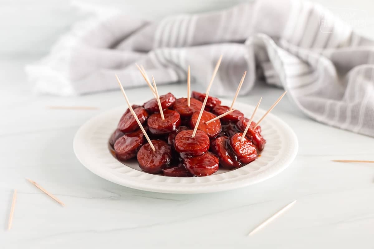 This Kielbasa appetizer is sweet, and savory, and packs a spicy punch! Perfect little bites for game day, holiday buffets, or any party! Kielbasa Appetizer on a plate with toothpicks.