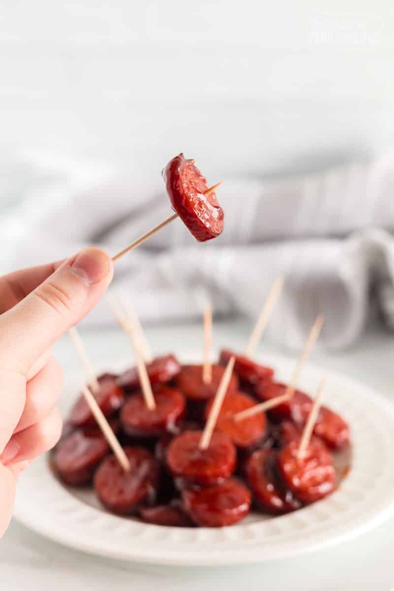 A toothpick with a round of kielbasa and a plate full of more in the background.