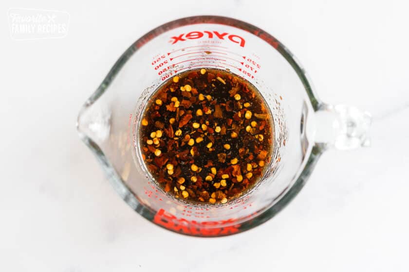Brown sauce with red pepper flakes in a glass measuring cup