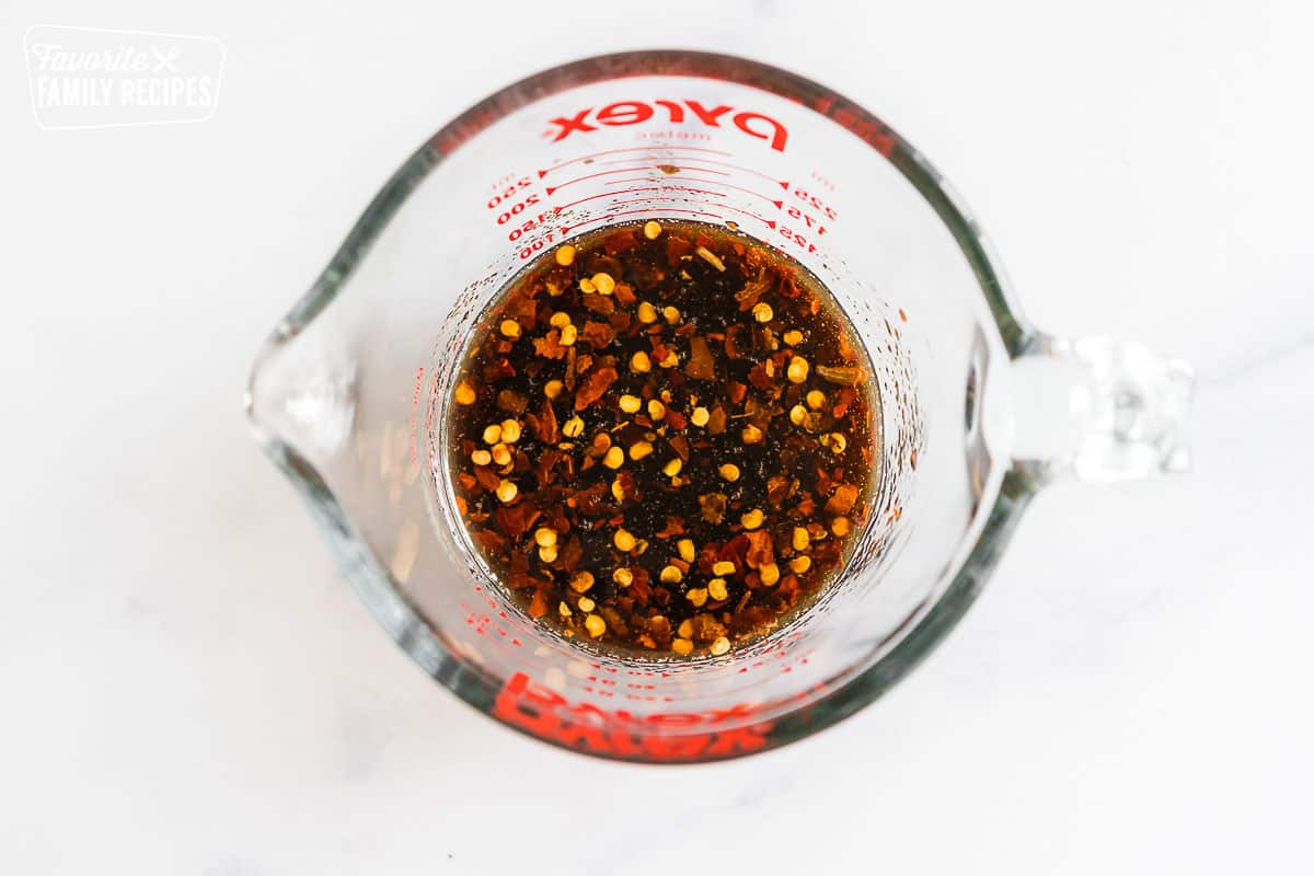 Brown sauce with red pepper flakes in a glass measuring cup