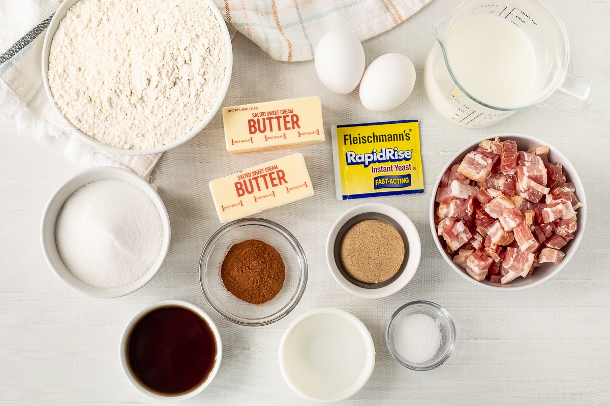 Ingredients to make Maple Bacon Monkey Bread including milk, bacon, yeast, butter, flour, eggs, sugar, maple syrup, cinnamon, salt, brown sugar and water.