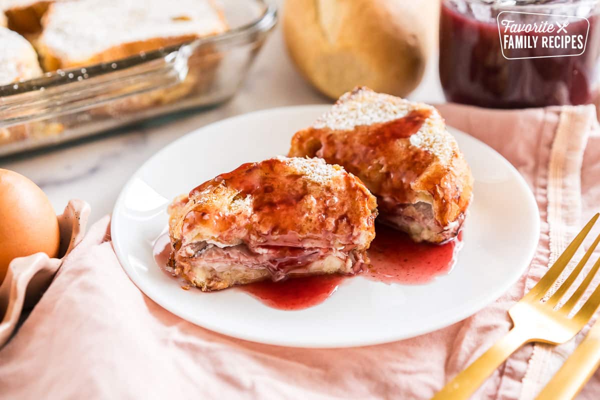 A slice of monte cristo casserole on a plate topped with berry syrup and cut in half