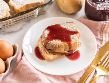 A slice of monte cristo casserole on a plate topped with berry syrup