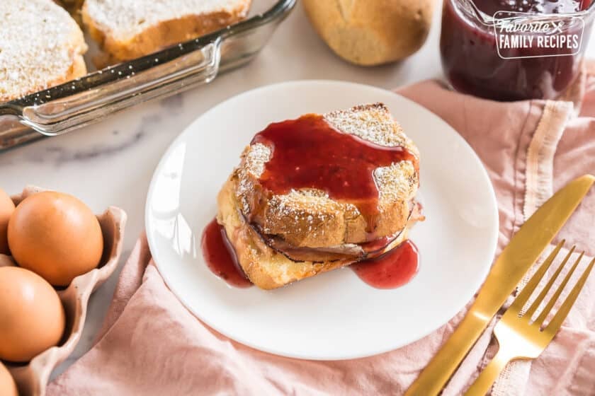 A slice of monte cristo casserole on a plate topped with berry syrup