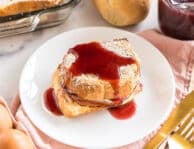 A slice of monte cristo casserole on a plate topped with berry syrup