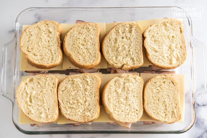 slices of French bread with cream cheese spread on them and topped with ham and turkey slices and swiss cheese and another slice of bread