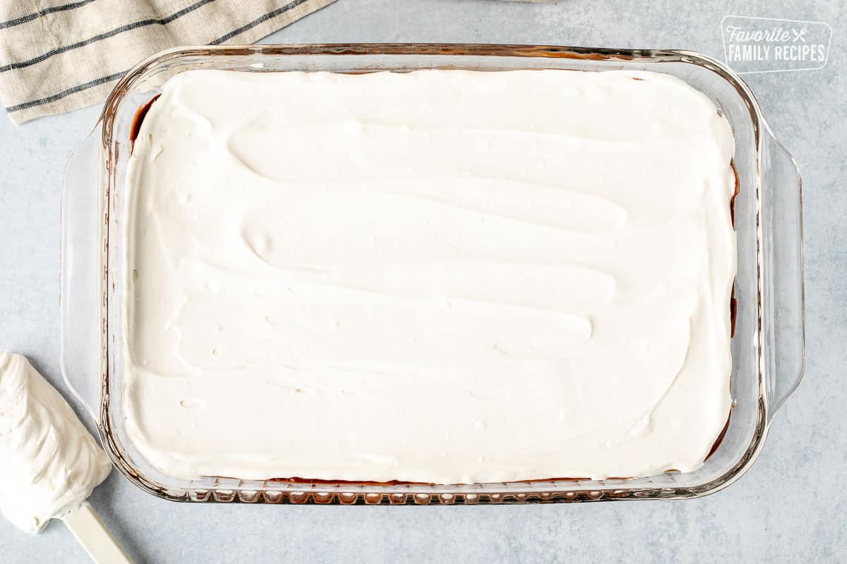Glass baking dish with Cool Whip layer spread on top.