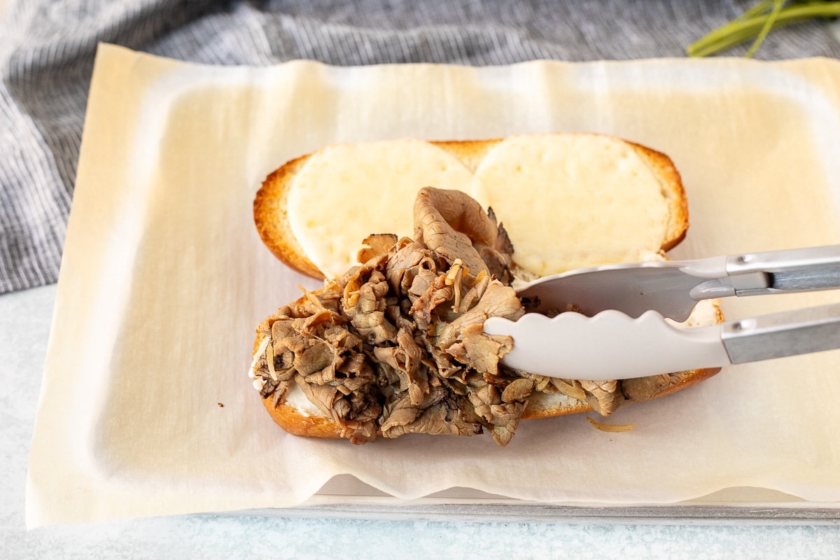 Placing sliced roast beef on a toasted French roll.