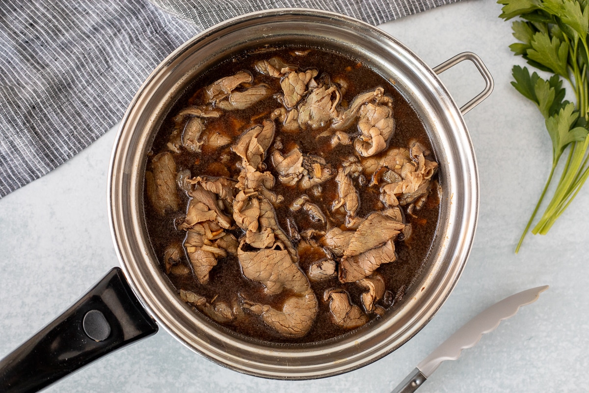 Pan with au jus and browned roast beef for French Dip Sandwiches.