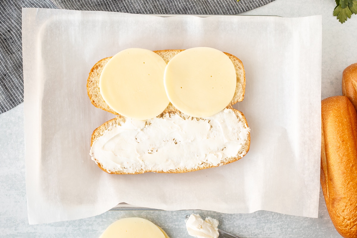 Cut open French roll with two slices of provolone cheese and spread cream cheese.