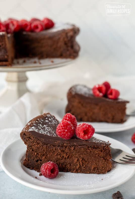 Two slices of Gluten Free Chocolate Cake next to cake stand with Gluten Free Chocolate Cake. Raspberries garnished on top.