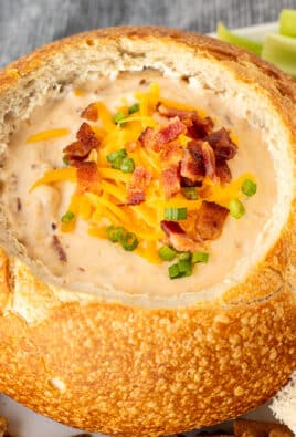 Close up of a bread bowl with warm bacon cheese dip topped with cheddar cheese, bacon and sliced green onions.