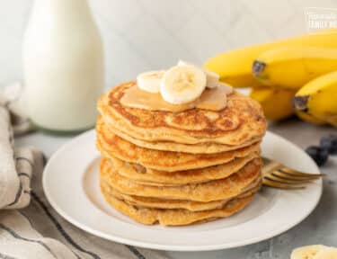 Stacked pile of Peanut Butter Pancakes with peanut butter and bananas.