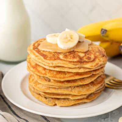 Stacked pile of Peanut Butter Pancakes with peanut butter and bananas.