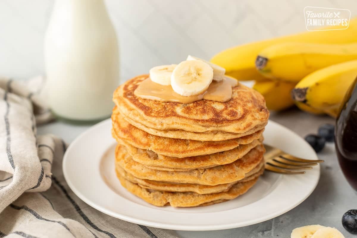 Stacked pile of Peanut Butter Pancakes with peanut butter and bananas.
