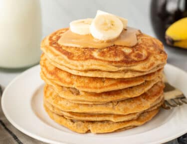 Stack of Peanut Butter Pancakes with peanut butter and sliced banana on top.