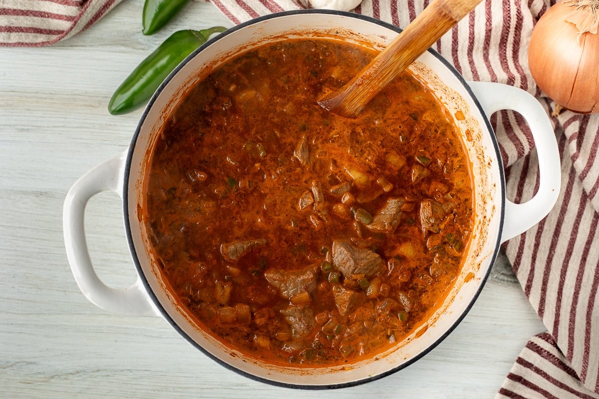 Simmering Texas Chili in a dutch oven and stirring with a wooden spoon.