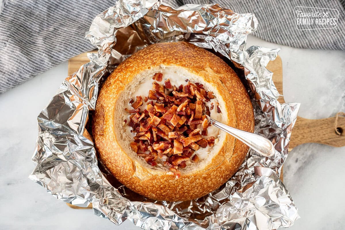 Adding bacon on top of the warm bacon cheese dip in a sour dough bread bowl.
