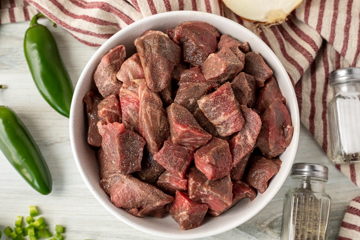 Bowl of cut beef in cubes seasoned with salt and pepper.