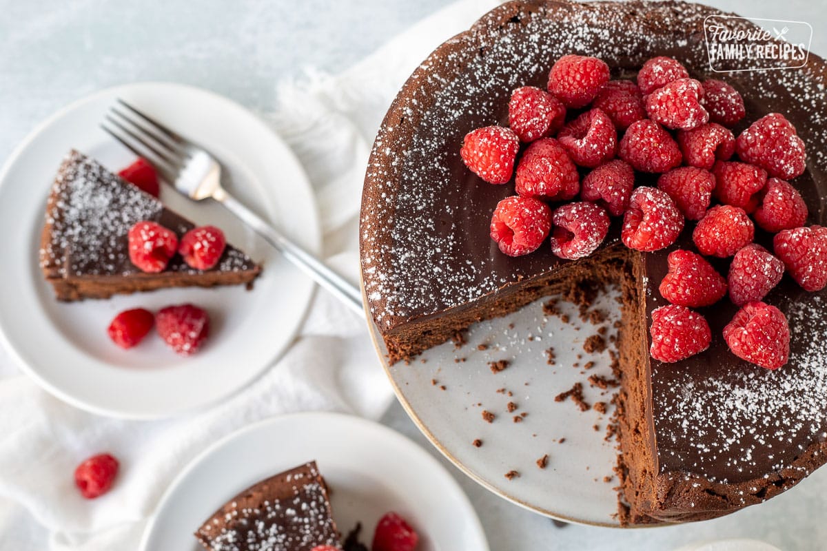 Whole Gluten Free Chocolate Cake with raspberries on top. Slice in the distance.