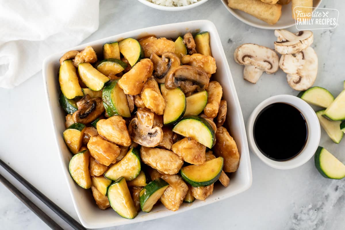 Dish of Panda Express Mushroom chicken. Soy sauce, mushrooms, spring rolls, rice and zucchini on the side.