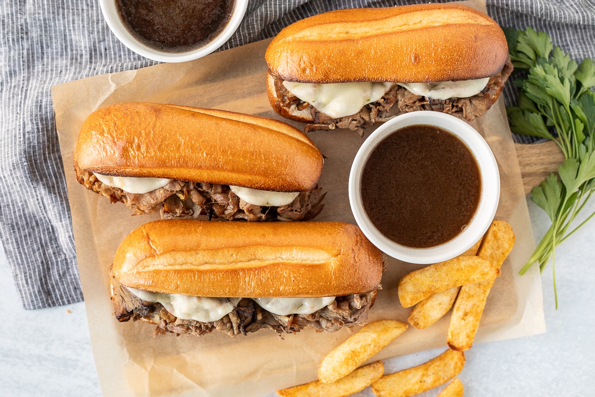 Three French Dip Sandwiches with fries and bowls of au jus.