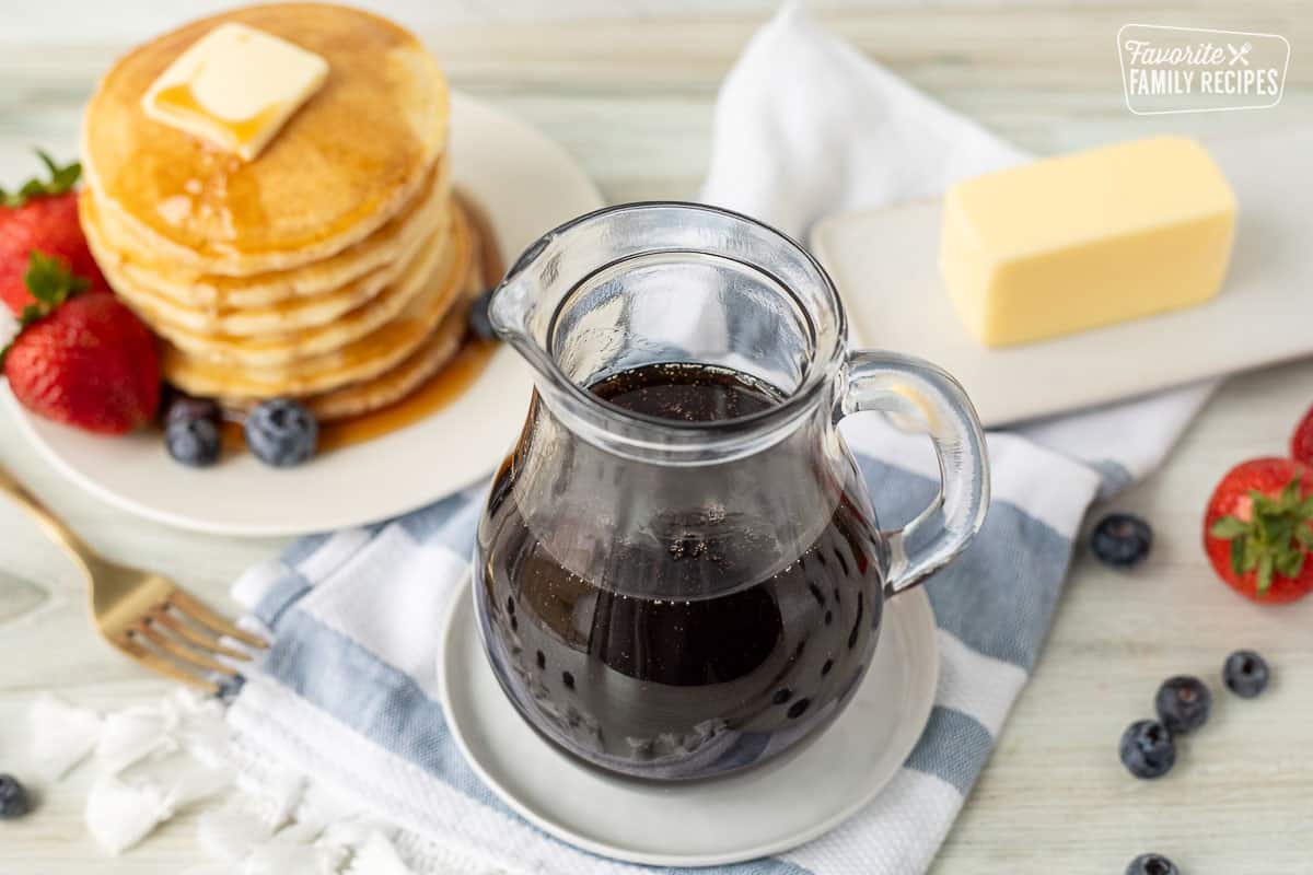 Overview of a jar with Homemade maple syrup, butter and a stack of pancakes with syrup.
