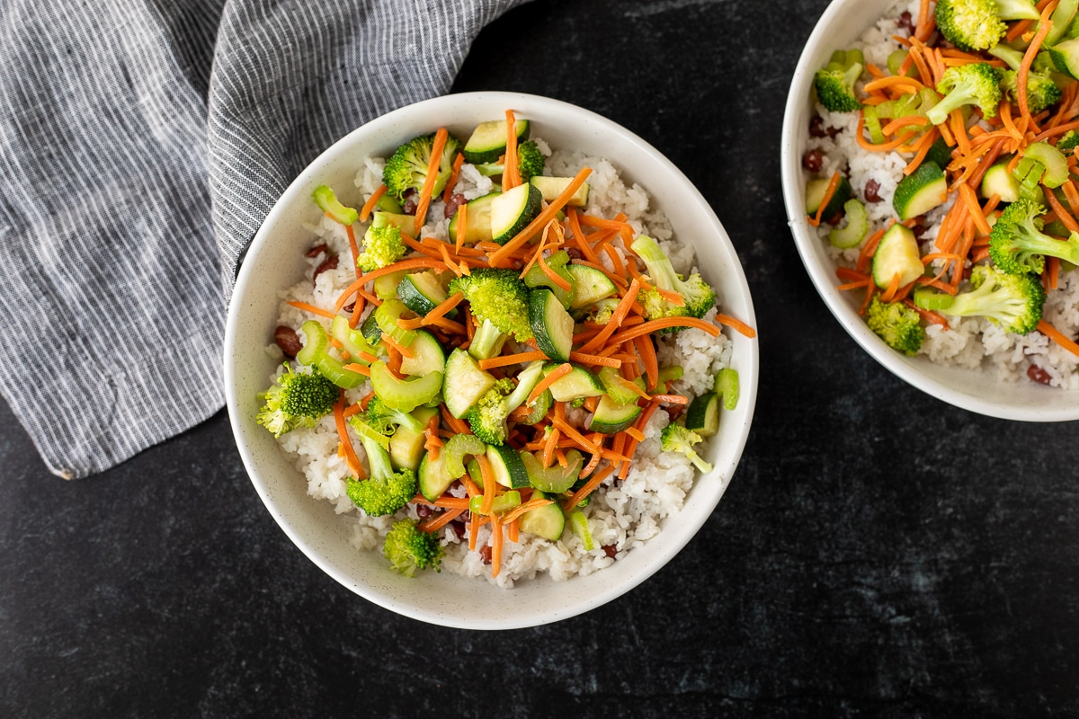 Two bowls of rice topped with steamed vegetables.