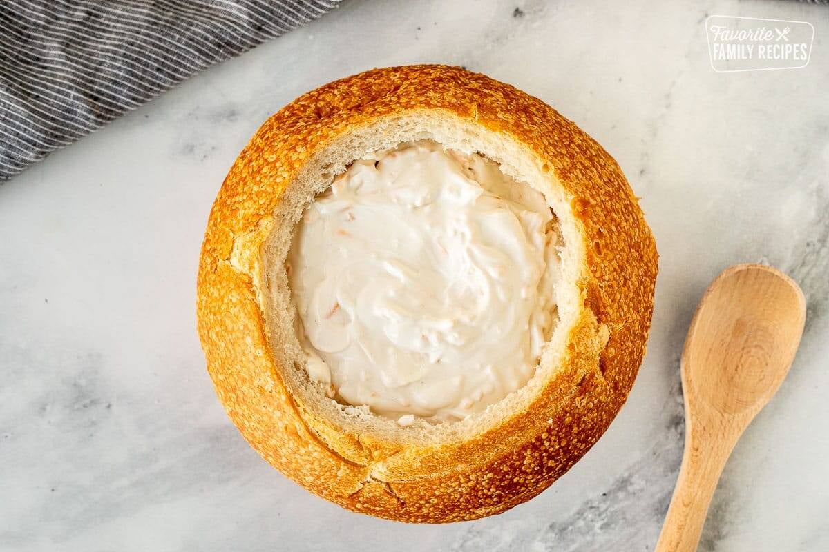 Bread bowl with Warm Bacon Cheese Dip and a wooden spoon on the side.