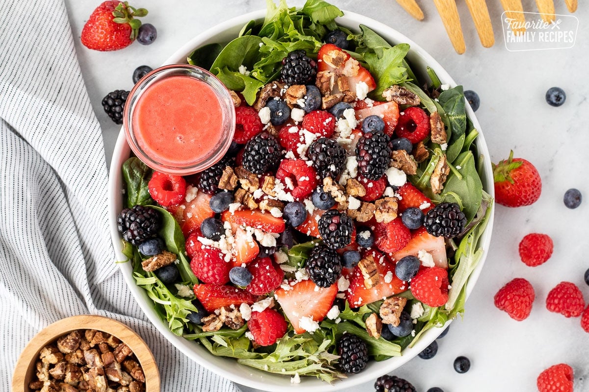 Salad bowl with Nuts About Berries Salad with a cup of raspberry dressing on the side.