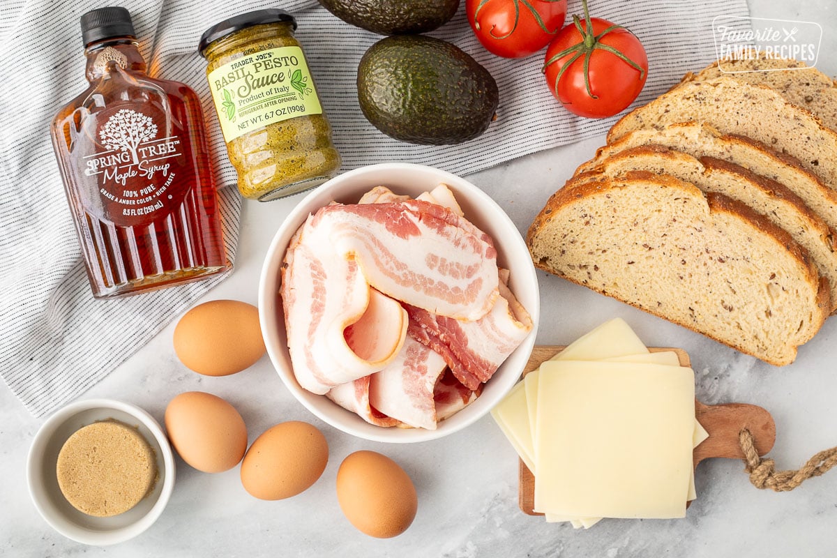 Ingredients to make Avocado Bacon and Egg Sandwich (Bam Sammy) including bacon, Sourdough grain bread, tomatoes, avocado, pesto, maple syrup, eggs, brown sugar and mozzarella cheese.