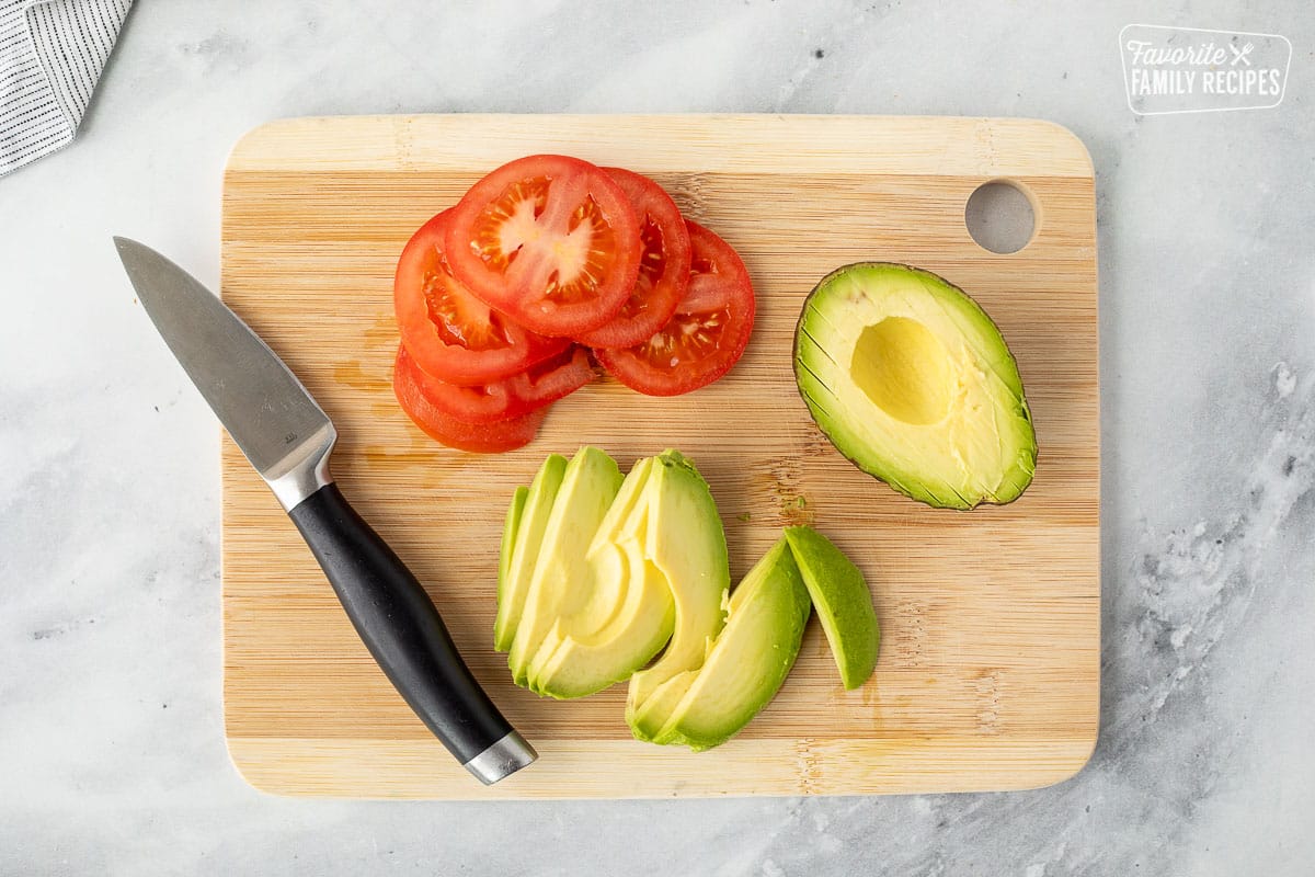 Cutting board with sliced avocado and sliced tomato.