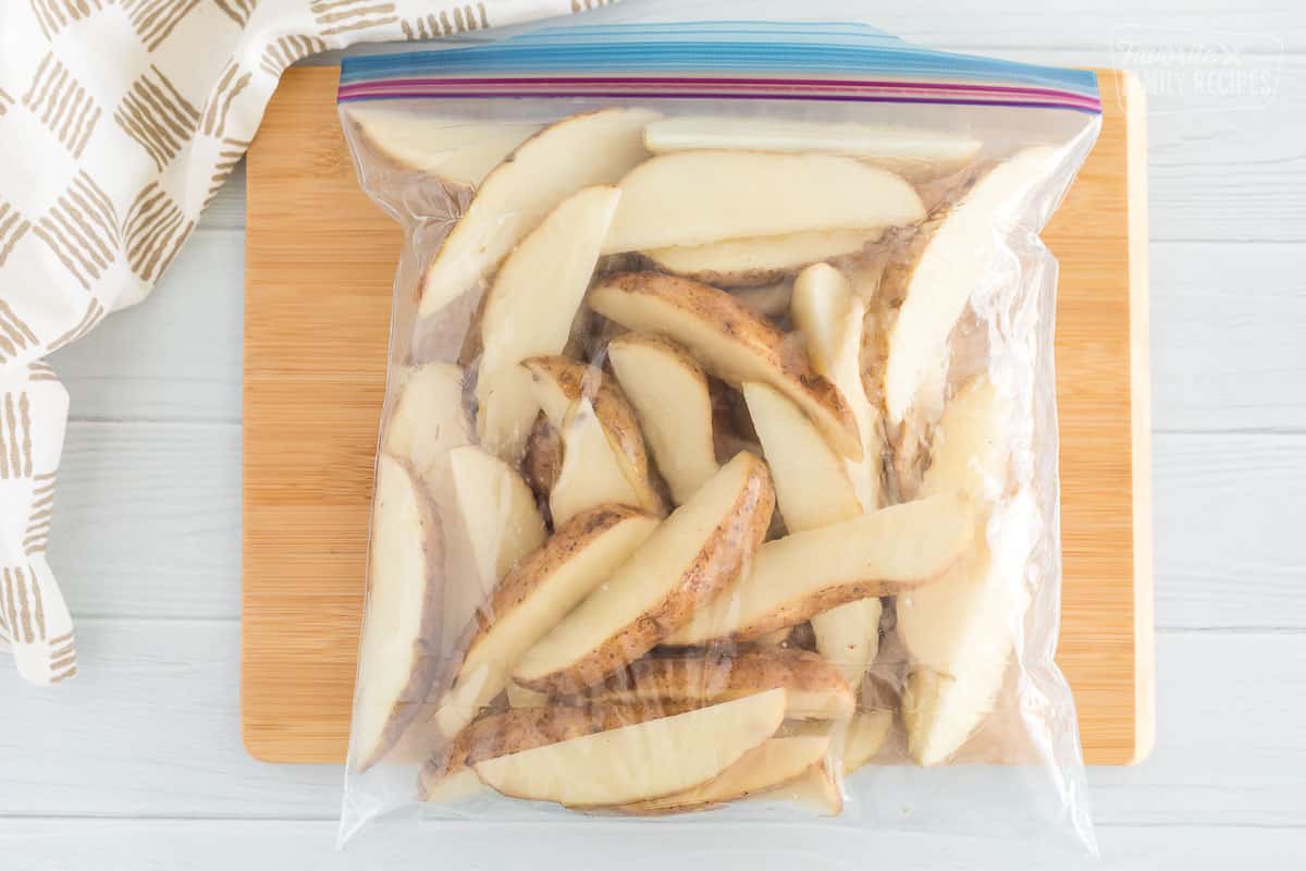 Wedges of potatoes that have been tossed in olive oil inside of a ziplock bag
