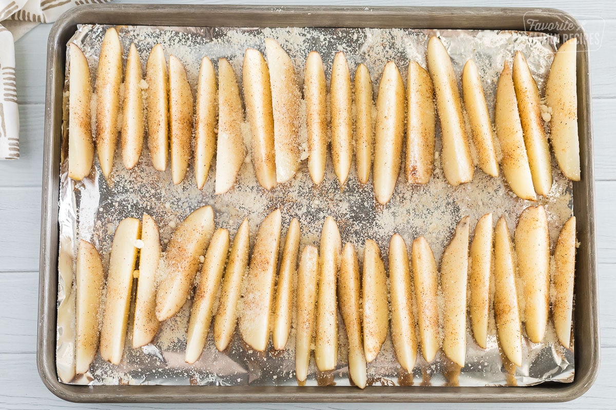 Wedges of potatoes laid out onto a cookie sheet with foil and sprinkled with seasoning salt and parmesan cheese