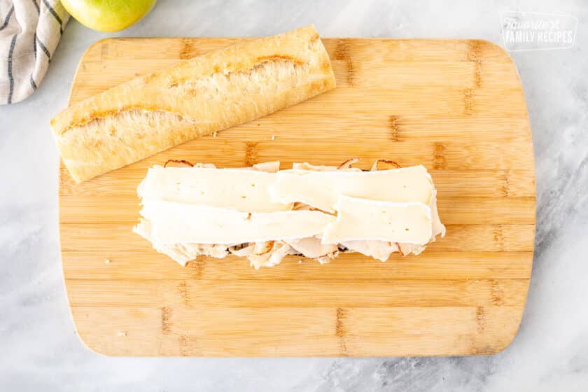 Placing slices of brie cheese on top of deli turkey breast.