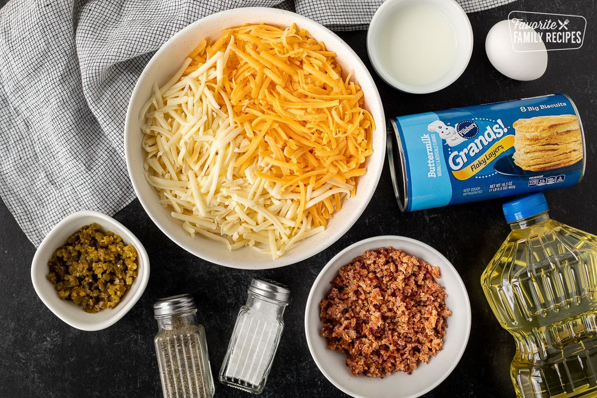 Ingredients to make Carthay Circle Fried Biscuits including shredded cheese, milk, egg, grands biscuits, oil, bacon, salt, pepper, diced jalapeños.