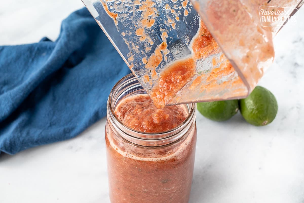Pouring blended salsa from a blender into a jar.