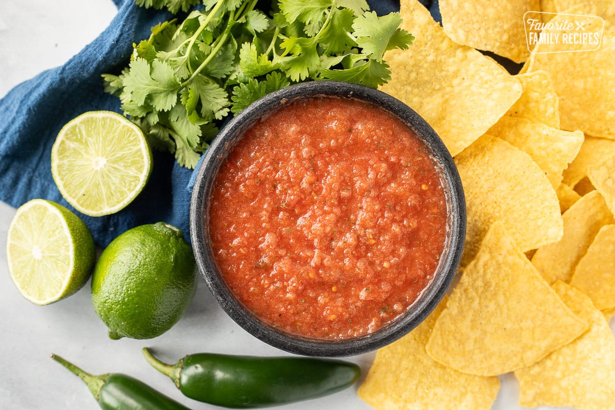 Bowl of Chili's copycat Salsa with tortilla chips, cilantro, limes and jalapeños.