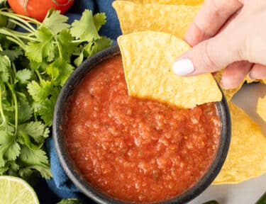 Hand dipping a tortilla chip in a bowl of Chili's Salsa.
