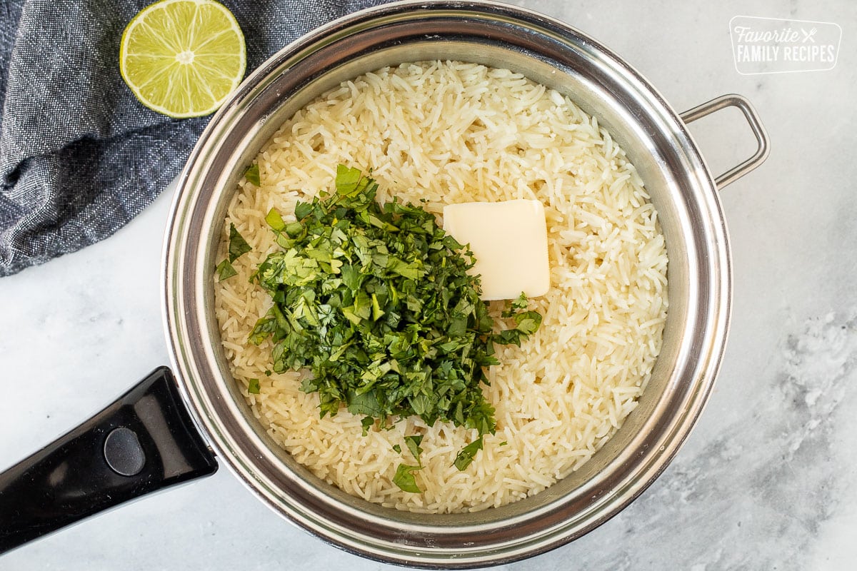 Fresh chopped cilantro, butter and lime juice on top of cooked rice in a saucepan.