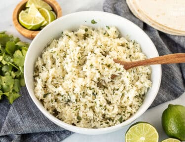 Chipotle Rice in a bowl with a spoon. Limes and cilantro on the side.