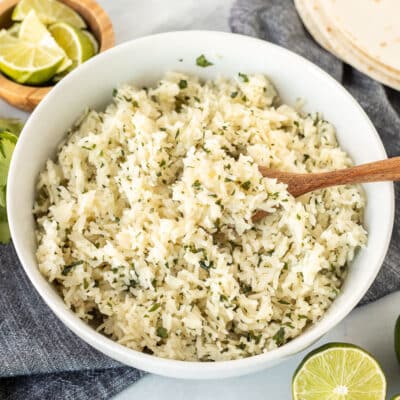 Chipotle Rice in a bowl with a spoon. Limes and cilantro on the side.