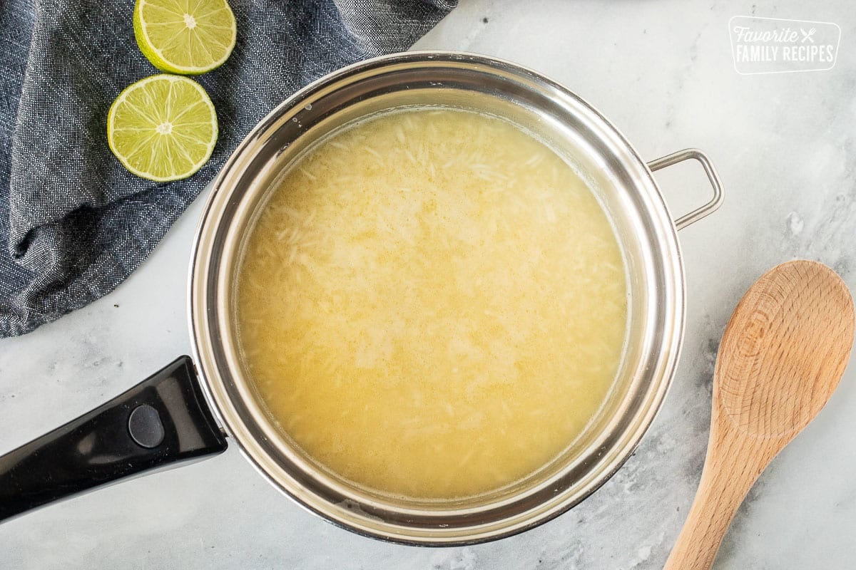 Saucepan of rice and chicken broth. Wooden spoon on the side.