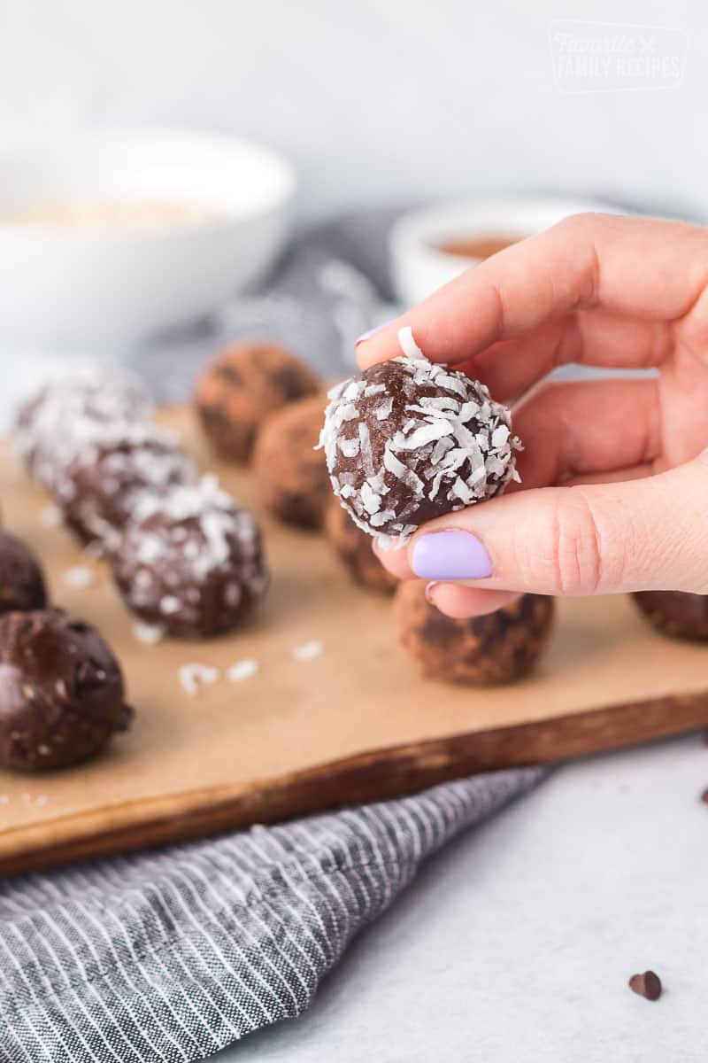 A chocolate protein ball covered in coconut being held up.