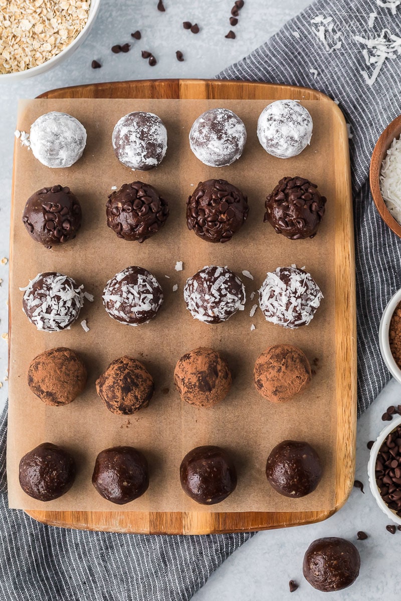 Chocolate protein balls on a board, rolled in various toppings such as cocoa powder, coconut, chocolate chips and powdered sugar.