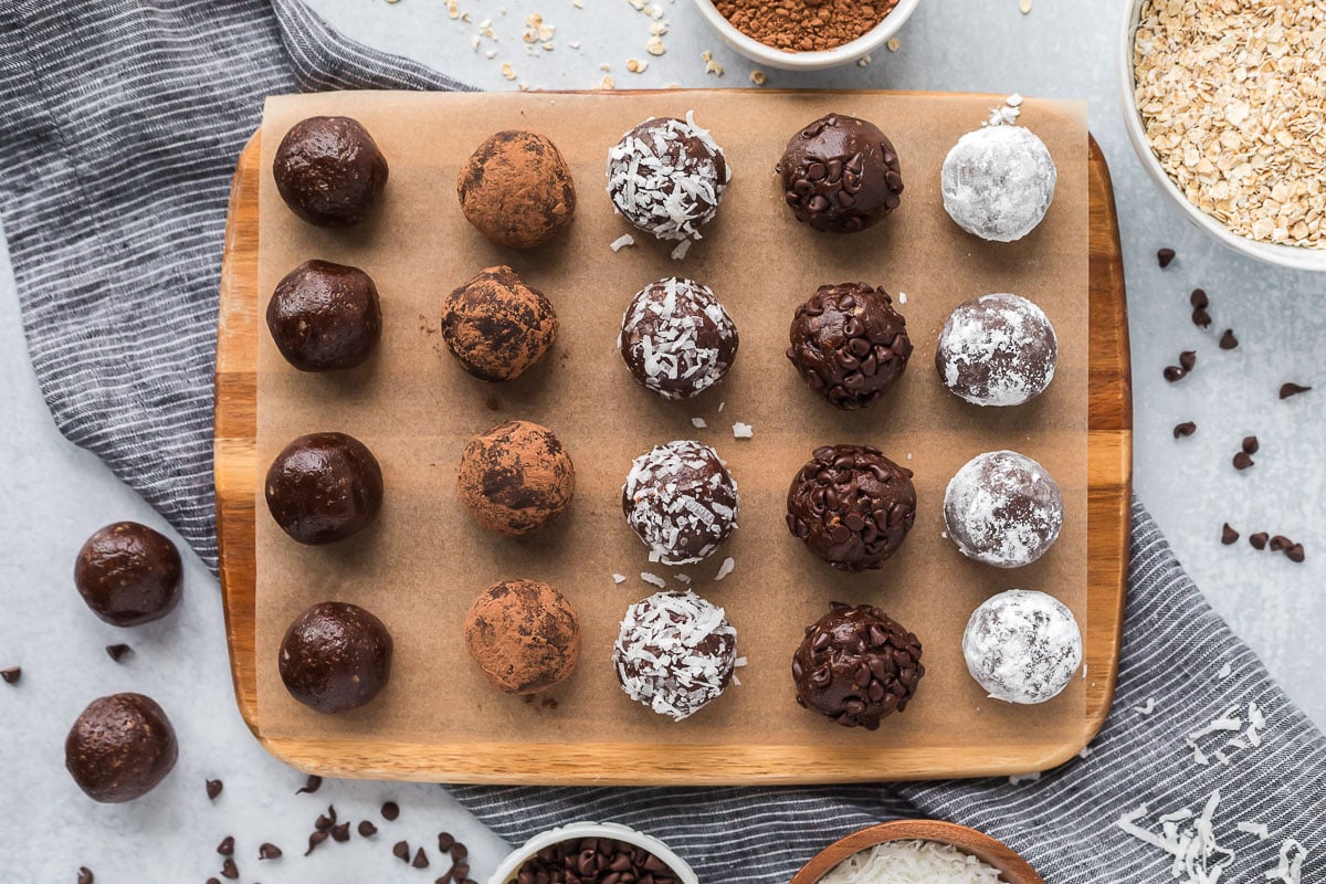 Chocolate protein balls on a board, rolled in various toppings such as cocoa powder, coconut, chocolate chips and powdered sugar