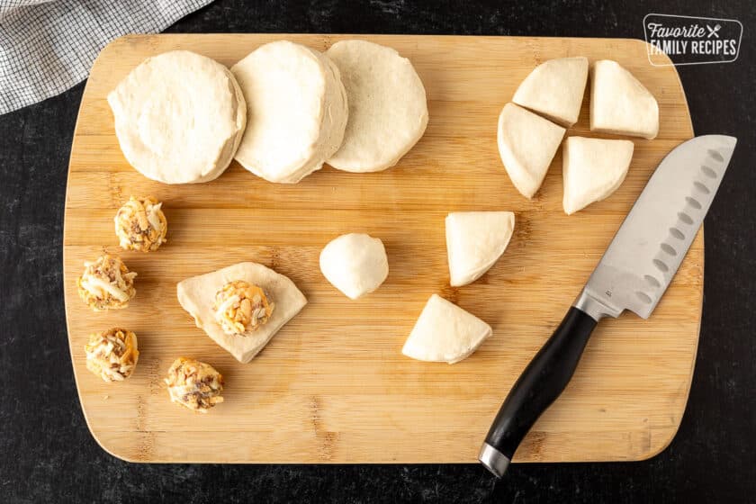 Cut biscuits and balls of cheese on a cutting board with a knife.