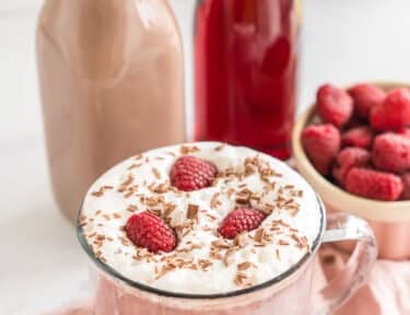 A mug of Dutch Bros Raspberry Hot Chocolate topped with soft top, raspberries, and chocolate shavings