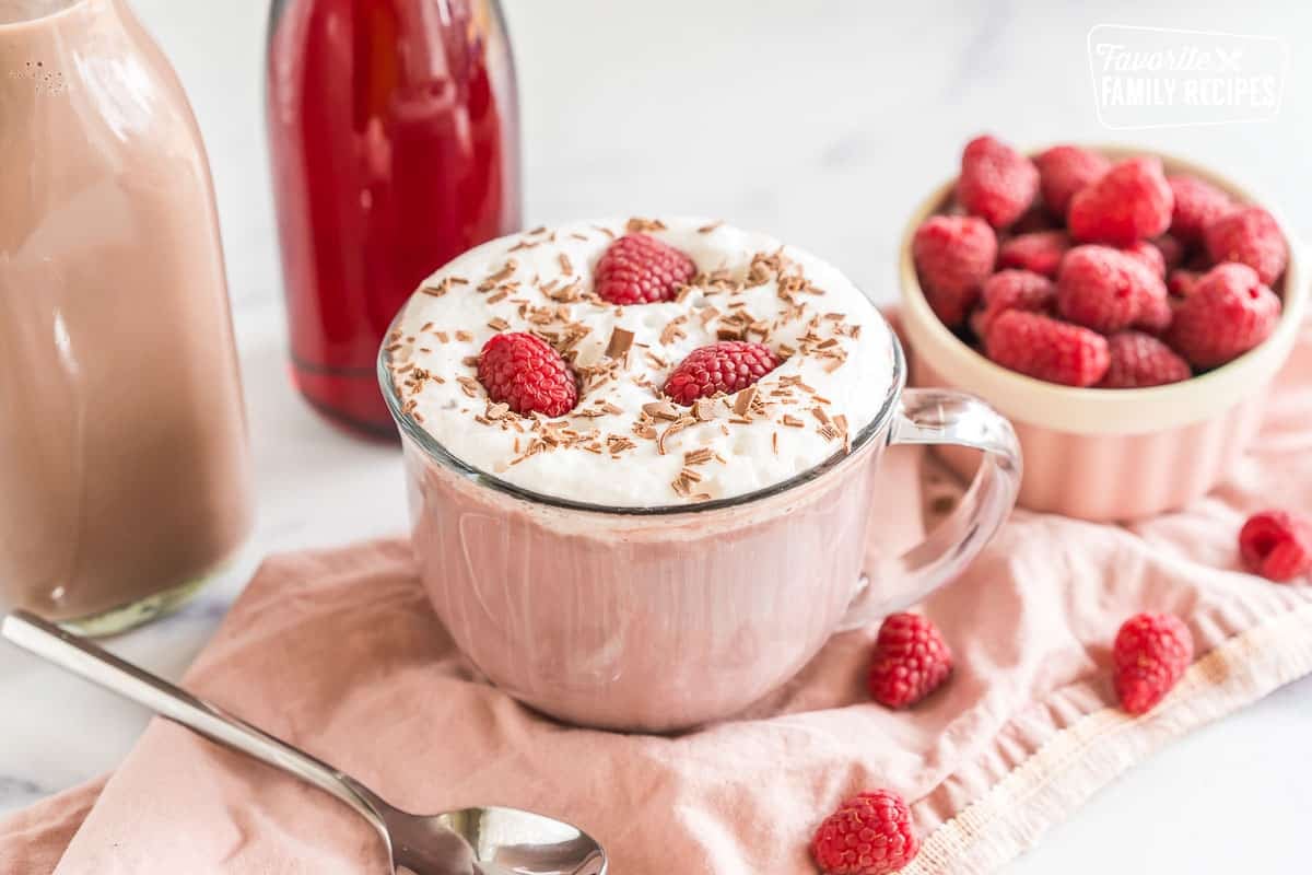 A mug of Dutch Bros Raspberry Hot Chocolate topped with soft top, raspberries, and chocolate shavings