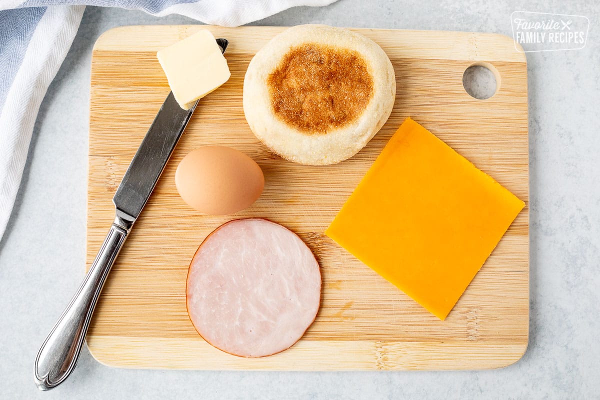 Ingredients to make an Egg McMuffin including English muffin, cheese, Canadian bacon, egg and butter.